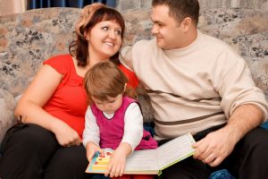 Married couple and little girl read book in a cosy room